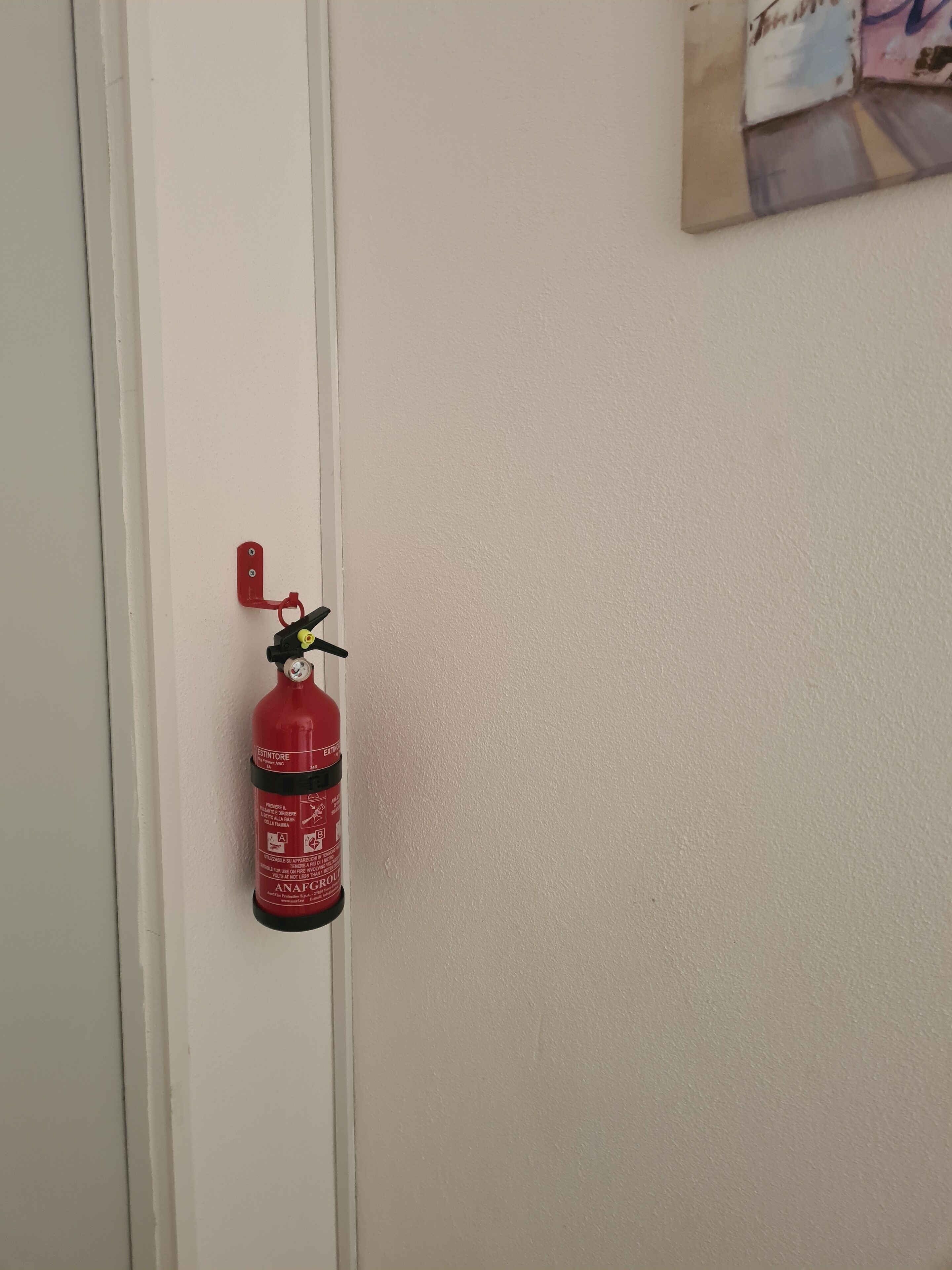 Un extincteur rouge fixé sur une porte blanche.