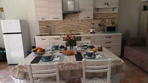 A kitchen with a dining table set for two, a refrigerator, a microwave, and a coffee maker. - STELLA MARINA holiday apartment, 450 meters from the sea, independent entrance (portoscuso)