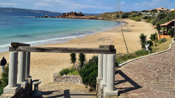 A coastal view with a sandy beach, a clear sky, and a stone pathway leading to a structure with columns. - STELLA MARINA holiday apartment, 450 meters from the sea, independent entrance (portoscuso)