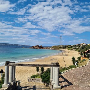 A coastal view with a sandy beach, a clear sky, and a stone pathway leading to a structure with columns. - STELLA MARINA holiday apartment, 450 meters from the sea, independent entrance (portoscuso)