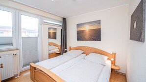 Un dormitorio con cama, lámparas de noche, una ventana con persianas, un radiador y un cuadro en la pared.