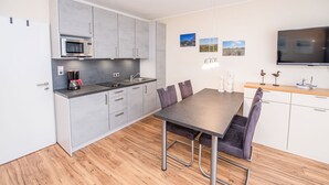 Cocina compacta con microondas, cafetera y comedor con mesa y sillas.