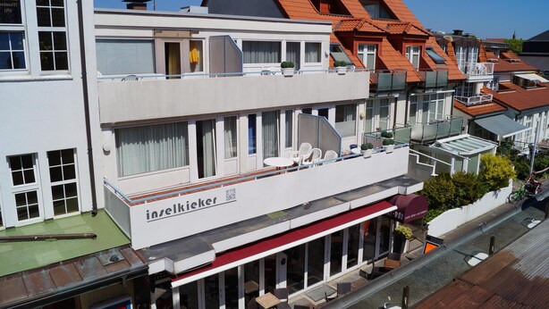 Un edificio de varios pisos con un restaurante en la planta baja, que cuenta con amplias ventanas y terraza.