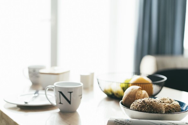 A breakfast setting with a white mug, a bowl of muffins, and a newspaper on a table.