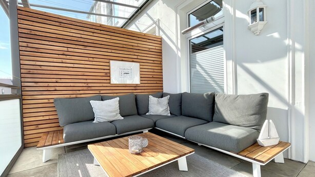 A modern living area with a sectional sofa, wooden slatted wall, and a wooden coffee table. - Haus Jantje Mö Wohnung 5 (Norderney)