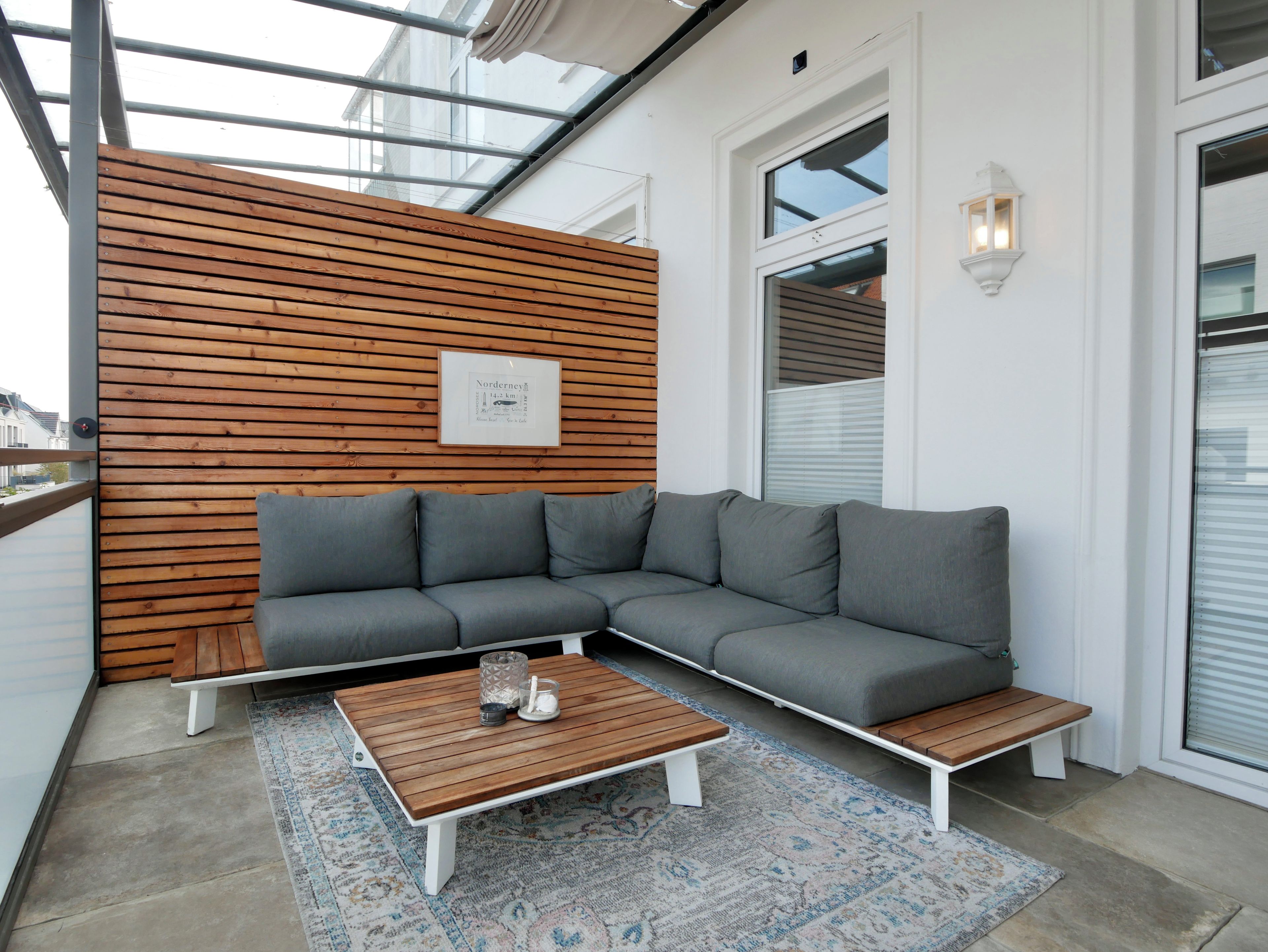 A modern outdoor seating area with a wooden slatted wall, a grey sectional sofa, and a wooden coffee table.