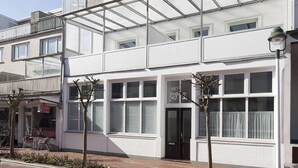 A white building with multiple windows and a glass balcony. - Haus Jantje Mö Wohnung 5 (Norderney)