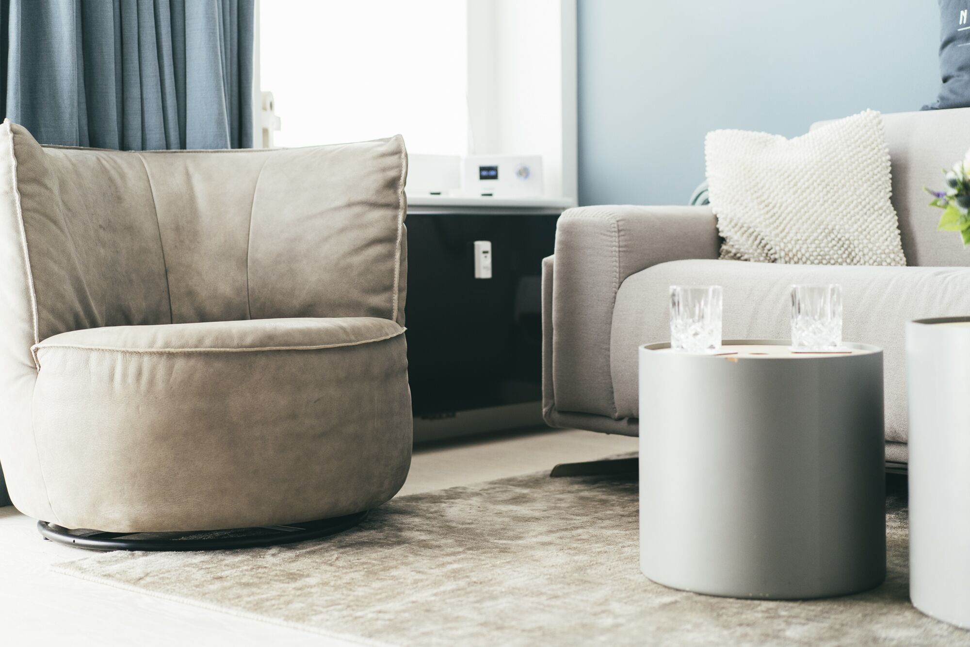 Una sala de estar moderna con un sillón beige, un reposapiés gris y un sofá blanco.