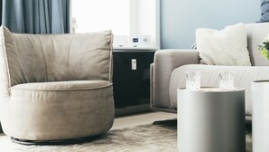 A modern living room with a beige armchair, a grey ottoman, and a white sofa. - Haus Jantje Mö Wohnung 5 (Norderney)