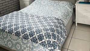 A bedroom with a bed, two nightstands, a window with curtains, a wall-mounted picture, and a tiled floor. - whalecome house Bongaree (Brisbane)