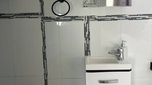 A bathroom with white tiles, a sink with a soap dispenser, and two towel rings. - whalecome house Bongaree (Brisbane)