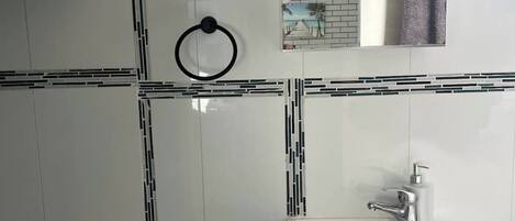 A bathroom with white tiles, a sink with a soap dispenser, and two towel rings.