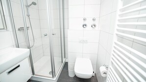 Et moderne badeværelse med bruseniche i glas, et hvidt toilet og en hvid vask.