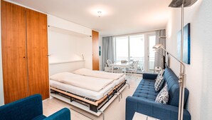 A modern hotel room with a bed, a sofa, a desk, and a balcony with a view. - Haus Meeresbrandung Wohnung 23 (Norderney)