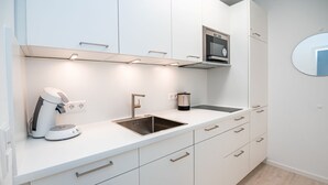 A modern kitchen with white cabinetry, a stainless steel sink, a coffee machine, and a microwave. - Haus Meeresbrandung Wohnung 23 (Norderney)