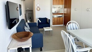 A modern living room with a sofa, a dining table, and a kitchen area with cabinets. - Haus Meeresbrandung Wohnung 23 (Norderney)