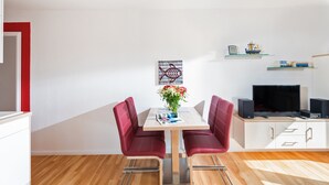 Un salon moderne avec une table à manger, des chaises rouges, un téléviseur et une bibliothèque.