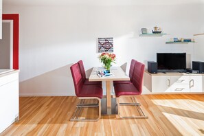 A modern living room with a dining table, red chairs, a TV, and a bookshelf. - Wohnung 26 / Kleiner Seebär (Norderney)