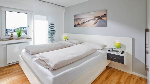 Une chambre à coucher moderne avec un grand lit, des tables de chevet, une fenêtre donnant sur un beau paysage et un tableau accroché au mur.