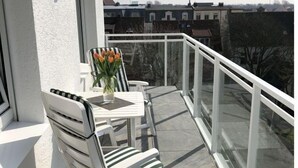 Un balcon avec une table et des chaises blanches, un vase de fleurs et une vue sur des bâtiments en arrière-plan.