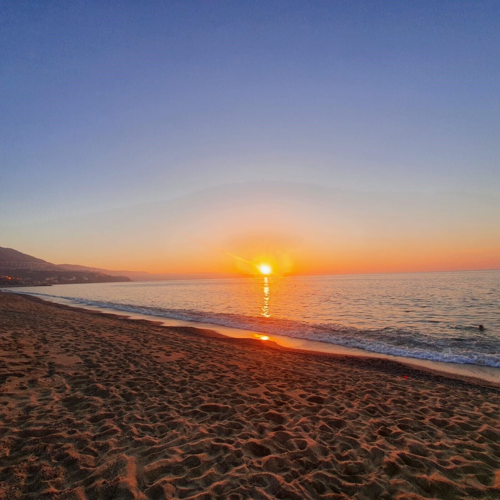Une plage où l’on peut admirer le coucher de soleil sur l’océan, avec un sol sablonneux et un ciel dégagé.