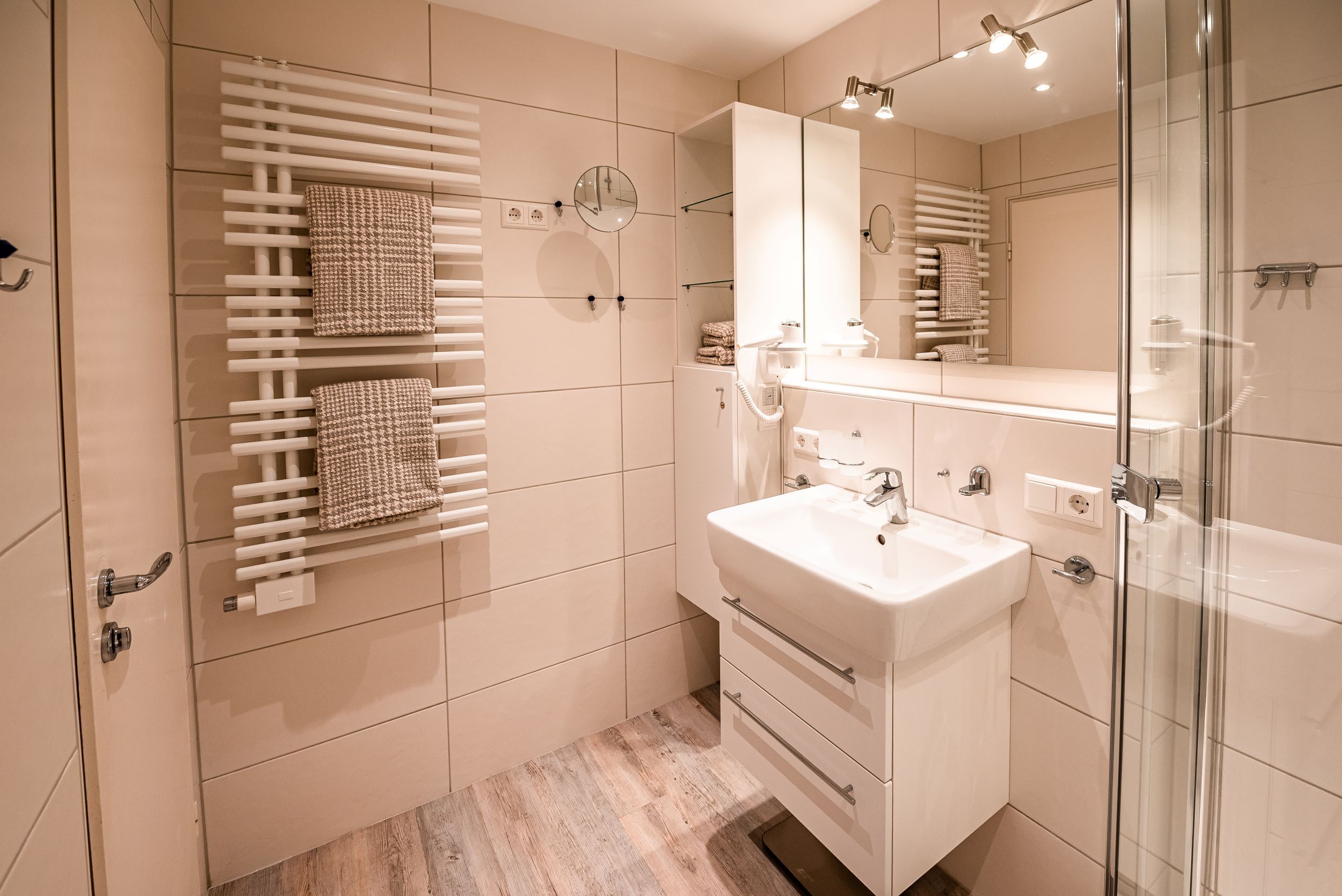 Un bagno moderno con un lavandino bianco, box doccia in vetro e porta asciugamani con asciugamani riposti ordinatamente.