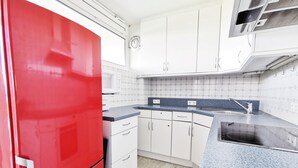 Una cocina con armarios blancos, un refrigerador rojo, una encimera azul y un microondas.