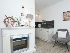 Een moderne keuken met een ingebouwde kookplaat, een eethoek met een grijze stoel, en een witte haardplank met decoratieve objecten.