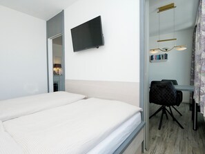 Een hotelkamer met een bed, een bureau met stoel, een aan de muur bevestigde televisie en een boekenkast met boeken.
