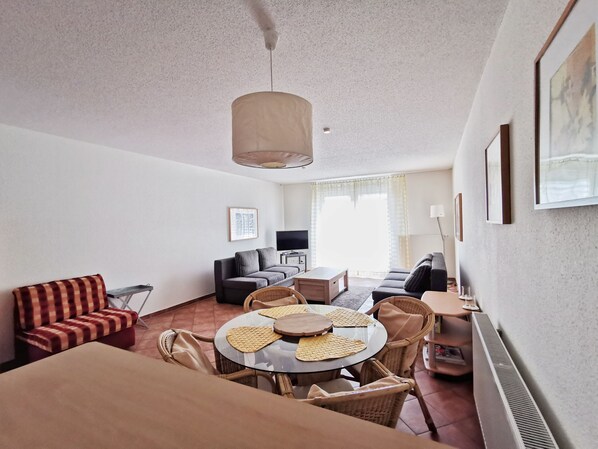 Un salon moderne avec une table à manger ronde, deux canapés, un téléviseur et un luminaire au plafond.