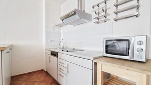 A kitchen with white cabinets, a stainless steel sink, a microwave, and a ventilation hood. - Villa Nordland Wohnung 6 (Norderney)