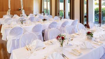 Een feestzaal met meerdere ronde tafels gedekt voor een formeel evenement, met witte tafelkleden, glazen en bloemstukken als decoratie.