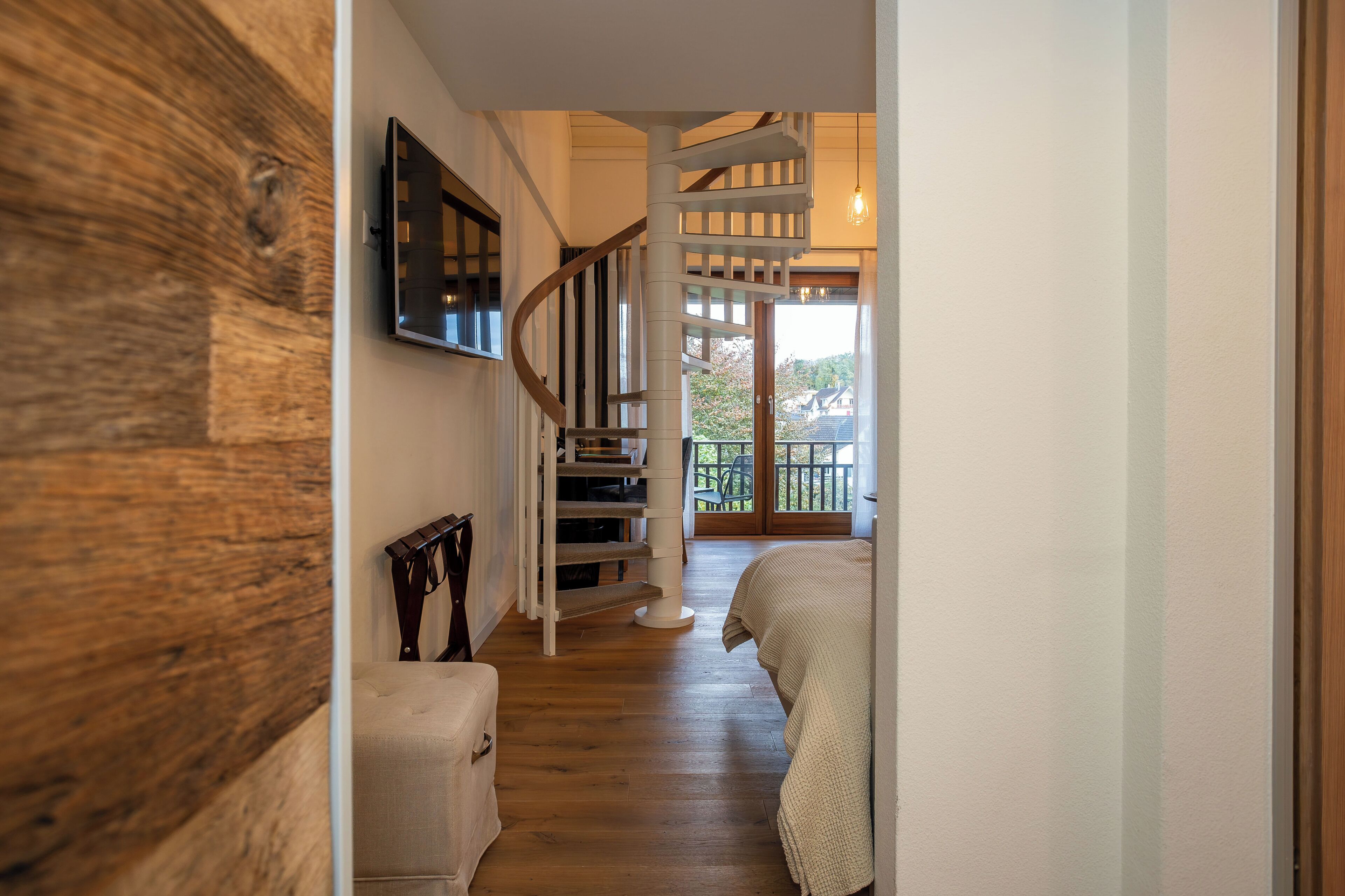 Un couloir avec un plancher en bois, un escalier, un lit et un téléviseur fixé au mur.