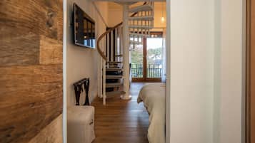 Un couloir avec un plancher en bois, un escalier, un lit et un téléviseur fixé au mur.