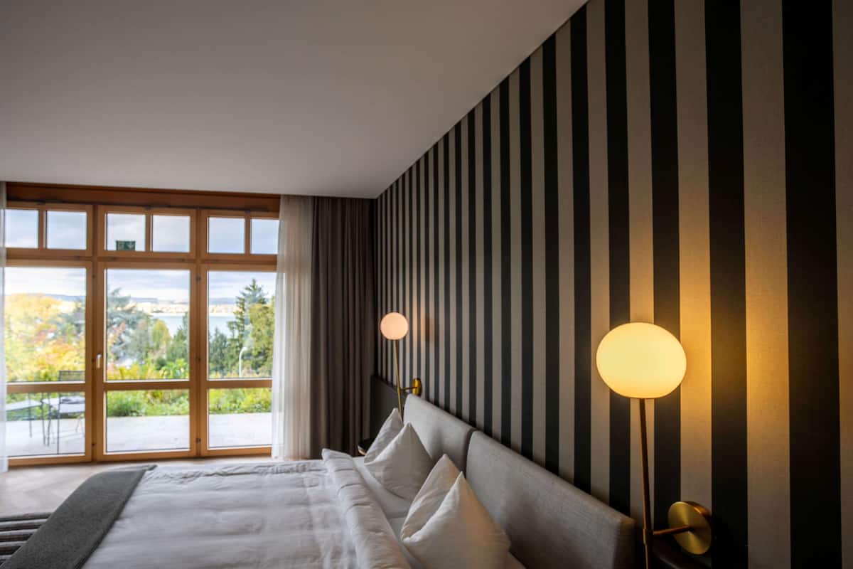 A modern hotel room with a large bed, striped wallpaper, and a view through a glass door.