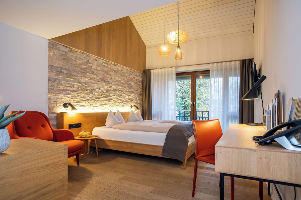A modern hotel room with a wooden ceiling, a large bed, a desk, and a dining area.