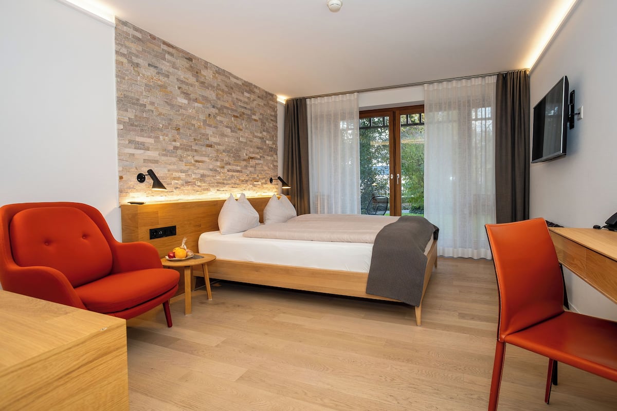 A modern hotel room with a bed, a desk, a chair, a small table, and a TV.