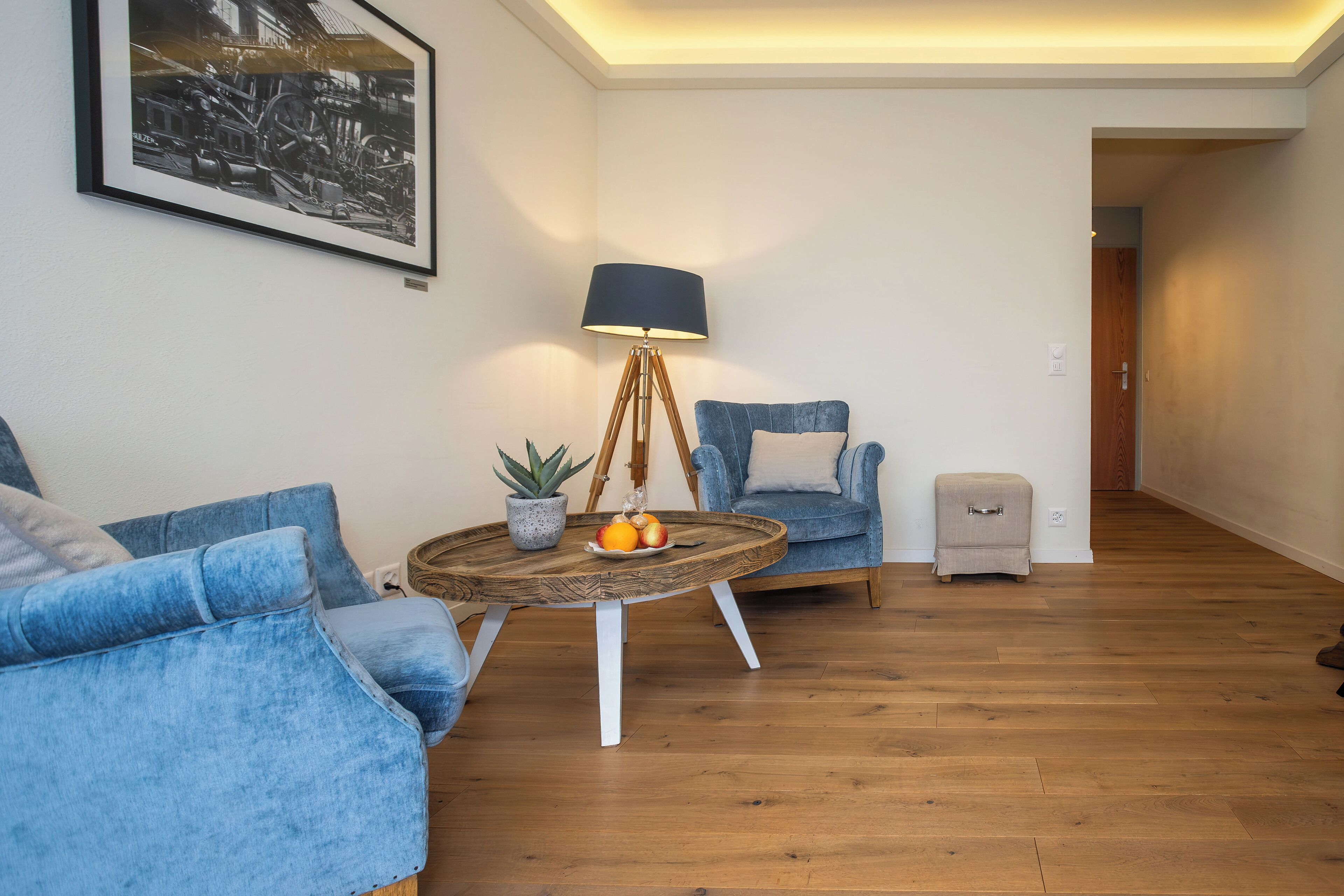 A living room with a blue sofa, a round coffee table with fruits, a lamp, and a framed picture on the wall.