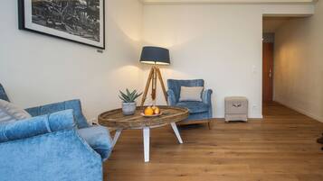 A living room with a blue sofa, a round coffee table with fruits, a lamp, and a framed picture on the wall.
