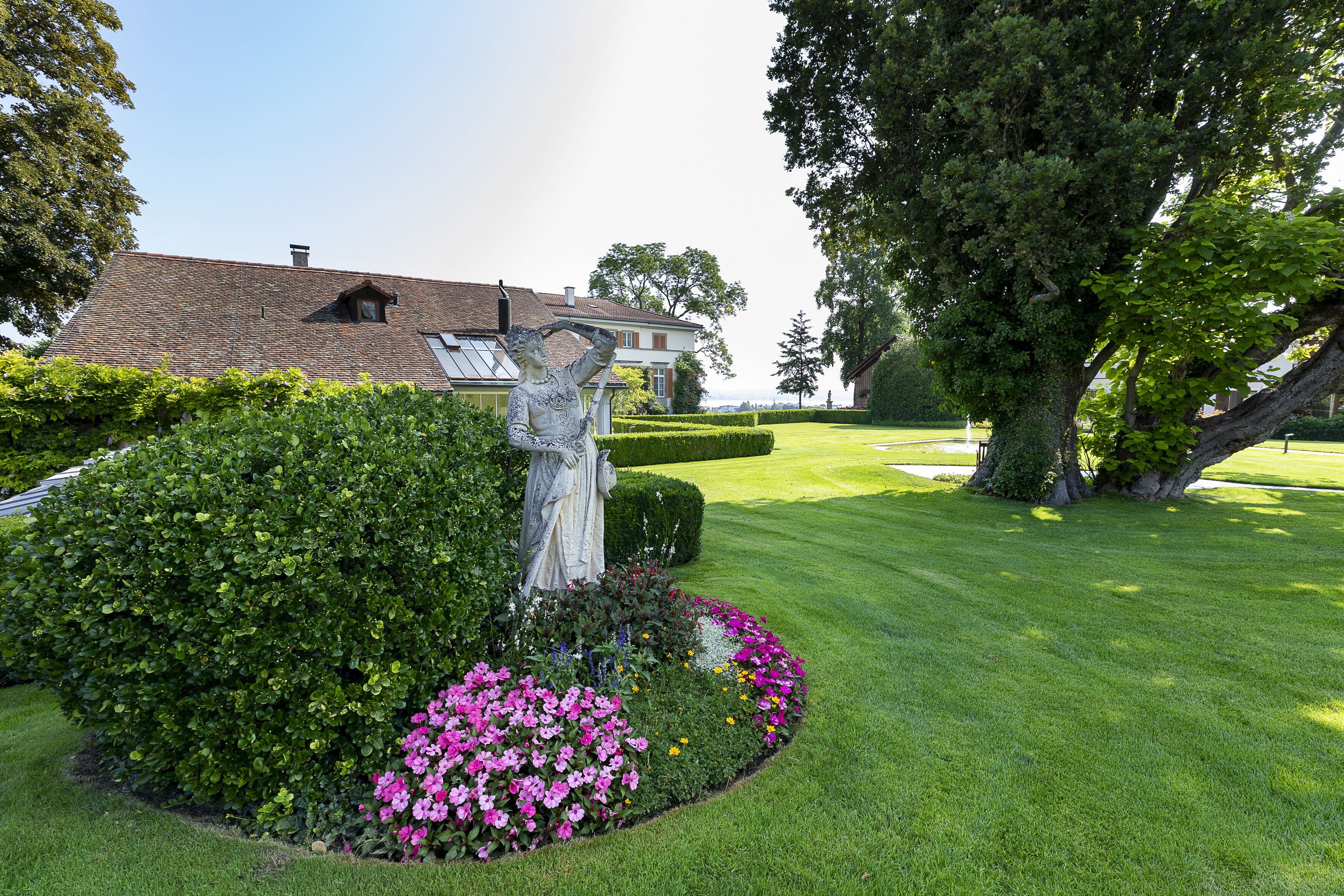 A well-maintained garden with a statue, neatly trimmed hedges, and a variety of flowers.
