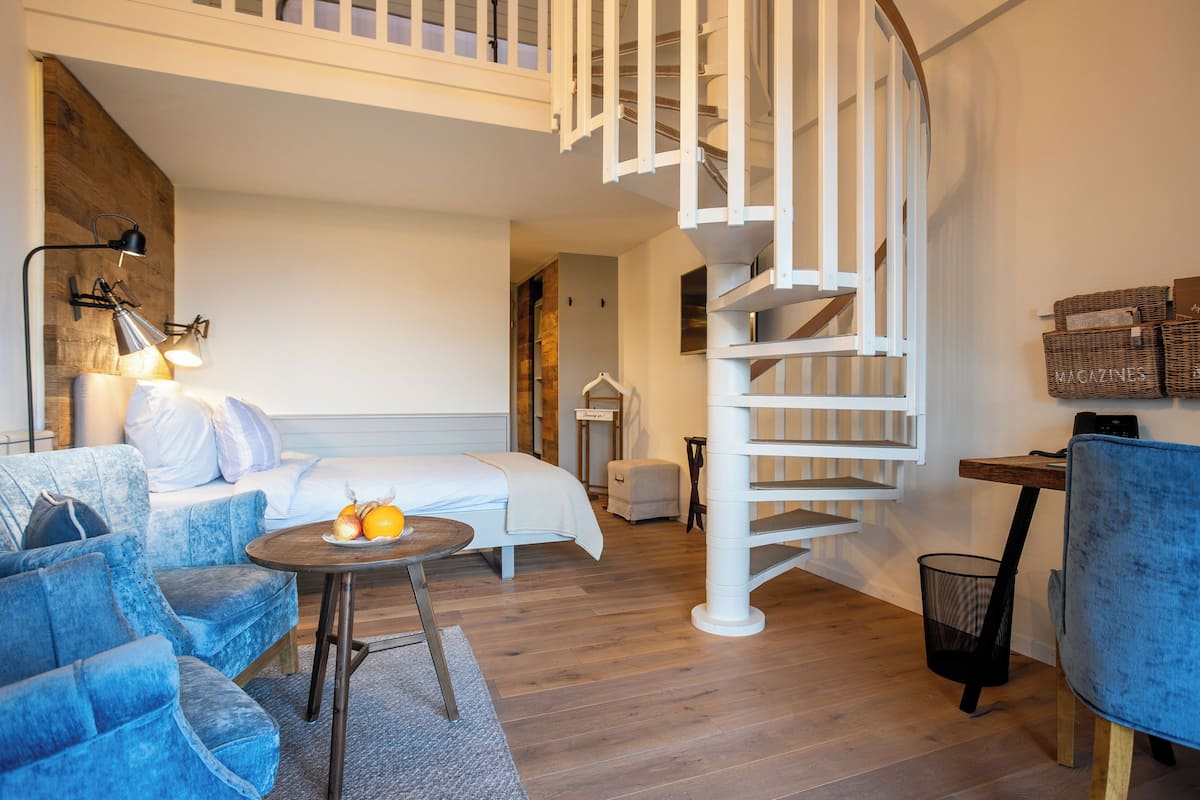 A modern living room with a spiral staircase, a sofa, a small table with fruit, and wicker baskets labeled "MAGAZINES" on the wall.