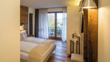 Een hotelkamer met een groot bed, een houten vloer, een balkon met uitzicht en een wandtelevisie.