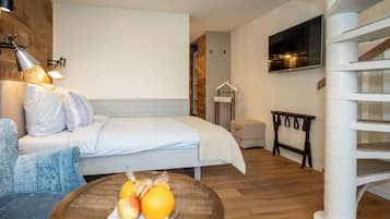 A bedroom with a bed, bedside table with fruit, a hanging coat rack, and a staircase.