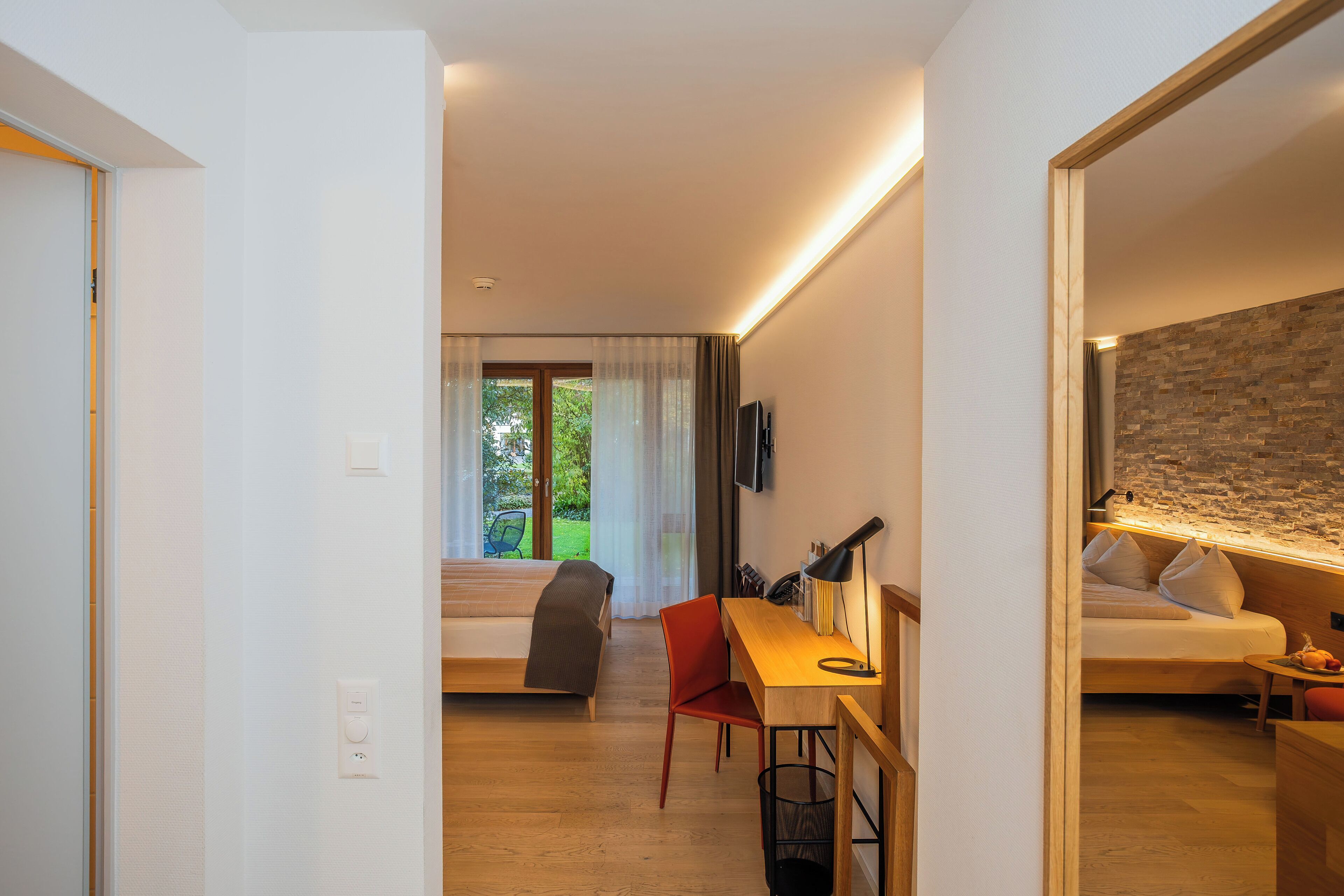 Un hotel moderno con un escritorio de madera, una silla roja, una cama y vistas a zonas verdes.
