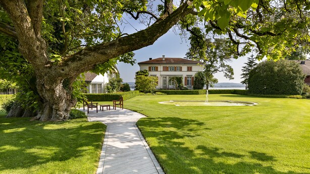 A well-maintained lawn with a wooden pathway leading to a building with a red roof. - LILIENBERG (Ermatingen)