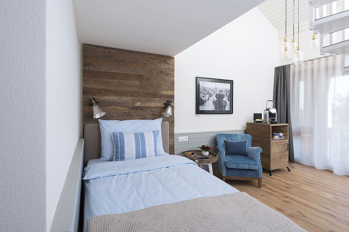 A modern bedroom with a bed, a chair, a nightstand, and a picture on the wall.