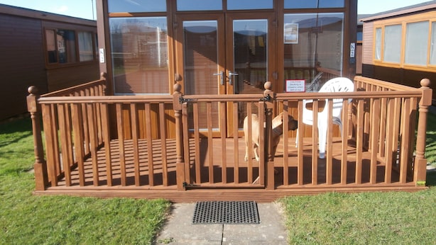 A wooden deck with a glass door leading to a covered area, a metal grate at the entrance, and a caution sign about slippery decking. - Inviting 2-bed Chalet in Mablethorpe (Mablethorpe)