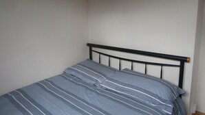 A small, single-bed room with a plain white wall and a simple black metal headboard. - Inviting 2-bed Chalet in Mablethorpe (Mablethorpe)