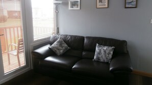 A dark leather sofa with two patterned pillows, a floor lamp, and three framed pictures on a light grey wall. - Inviting 2-bed Chalet in Mablethorpe (Mablethorpe)
