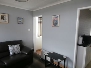 A living room with a black leather sofa, a small black table, and a wall with framed pictures.